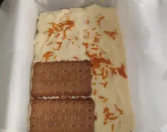 Step <p><span style="font-weight: normal;">Coloca en una fuente una o dos hojas de papel de hornear, en un plato hondo pon la leche y ves mojando las galletas por ambas caras, y colócalas en el molde forrado. Añade una virutas de naranja</span></p> illustration